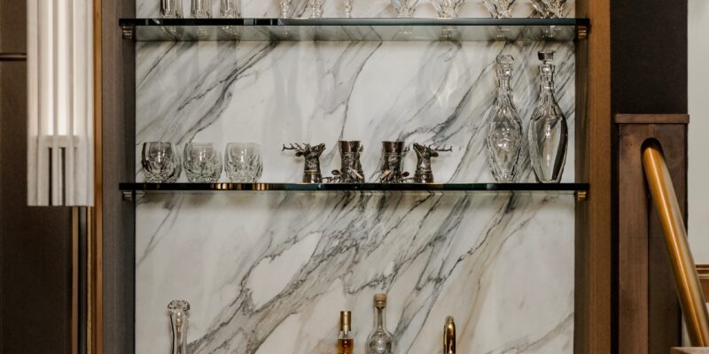 Gorgeous bar and game room with a white marble backsplash, warm woods, and elegant crystal glass chalices.