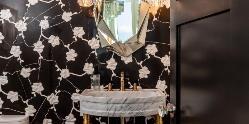 Stunning modern bathroom with floral wallpaper, crystal glass pendant lights, a freestanding gold and quartz vanity, and a geometric mirror.
