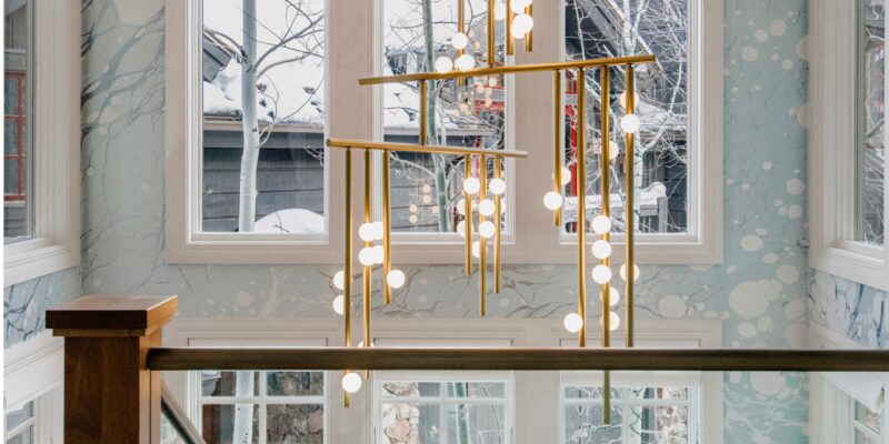 Luxurious Utah stairwell outfitted with warm woods, a sculptural gold chandelier with spherical LED glass diffusers, and a light blue organic wallpaper.